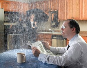 Frustrated man catching water from a leaking ceiling, illustrating common causes of roof leaks in a home