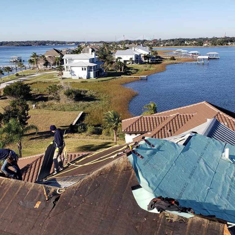 Prime Roofing technician installing a standing seam metal roof on a Jacksonville waterfront home with private dock and boathouse