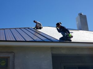 Two Prime Roofing employees aligning metal panels on roof