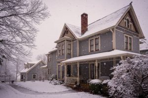 Victorian home with snow on roof representing winter roofing conditions