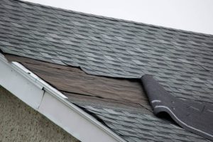 Torn shingles hanging off roof showing damage
