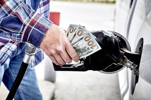Man refilling gas tank holding cash, illustrating rising gas prices affecting roofing costs