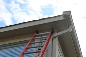 Ladder against house showing gutter system — highlights problems caused by clogged gutters
