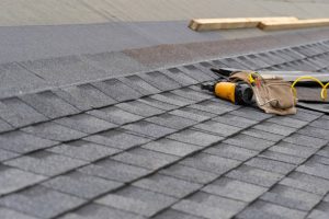 Toolbelt and nail gun on sloped asphalt shingle roof during essential roofing components installation