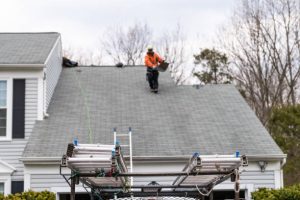 Roofer inspecting asphalt shingle roof on a garage with worker van and ladders nearby