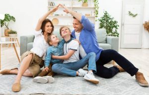 Young family at home with parents forming a roof shape, illustrating how to transfer roof warranty when selling a house.