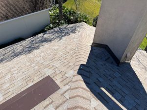 Newly installed Owens Corning Duration Amber shingles with black step flashing around a stucco chimney.
