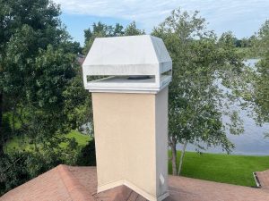 Close-up of a stucco chimney with a weathered metal cap and aging shingles on a home in Sawgrass, FL.